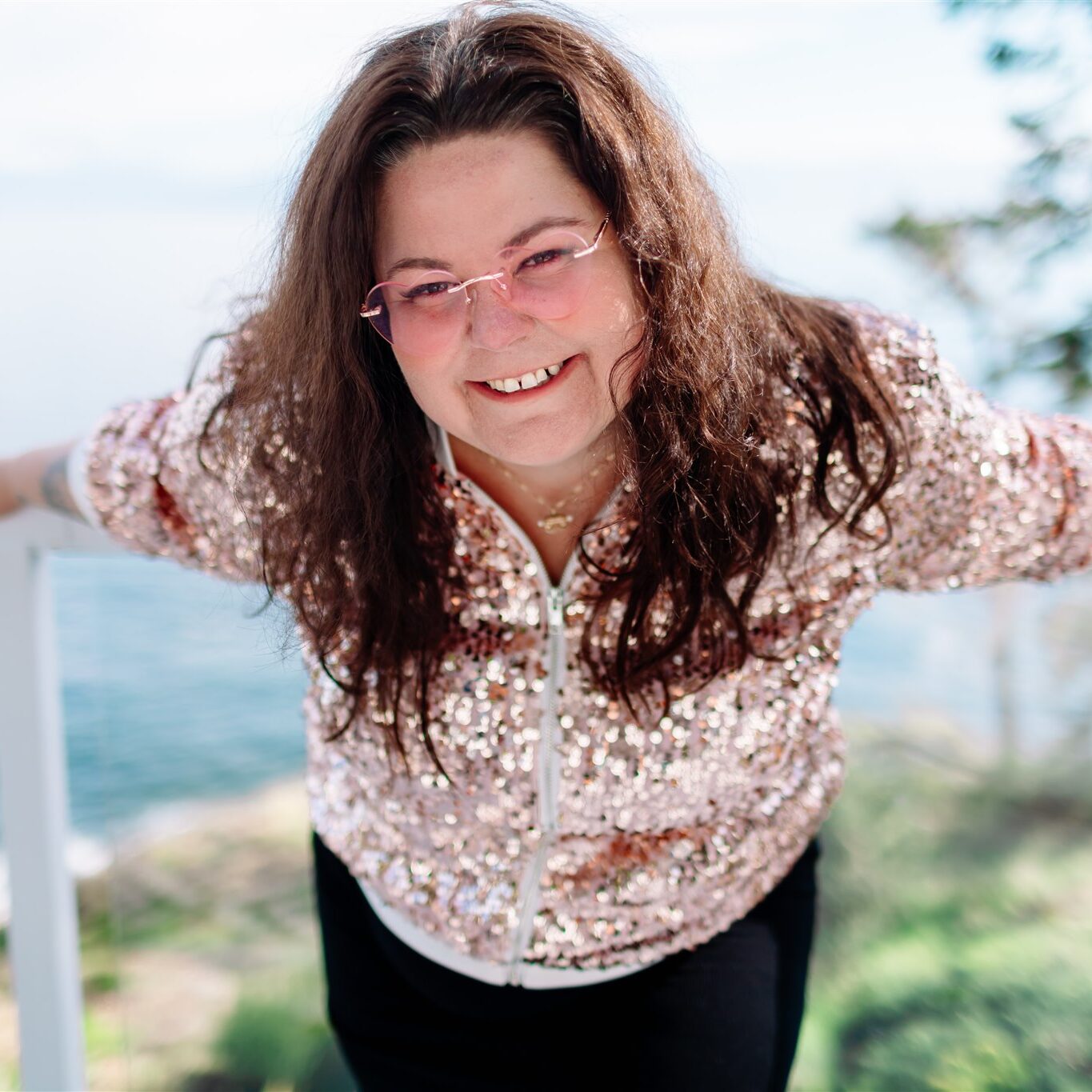 Crystal Adair-Benning laughing by the ocean in her pink sparkle jacket and pink glasses