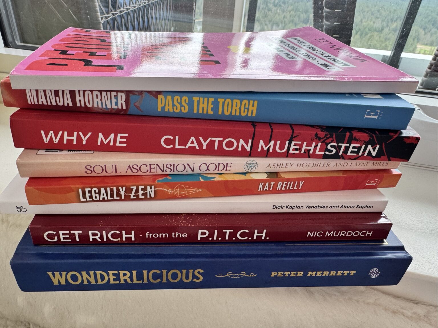 Spines of 8 books ghostwritten or coached by Crystal Adair-Benning, stacked on a windowsill