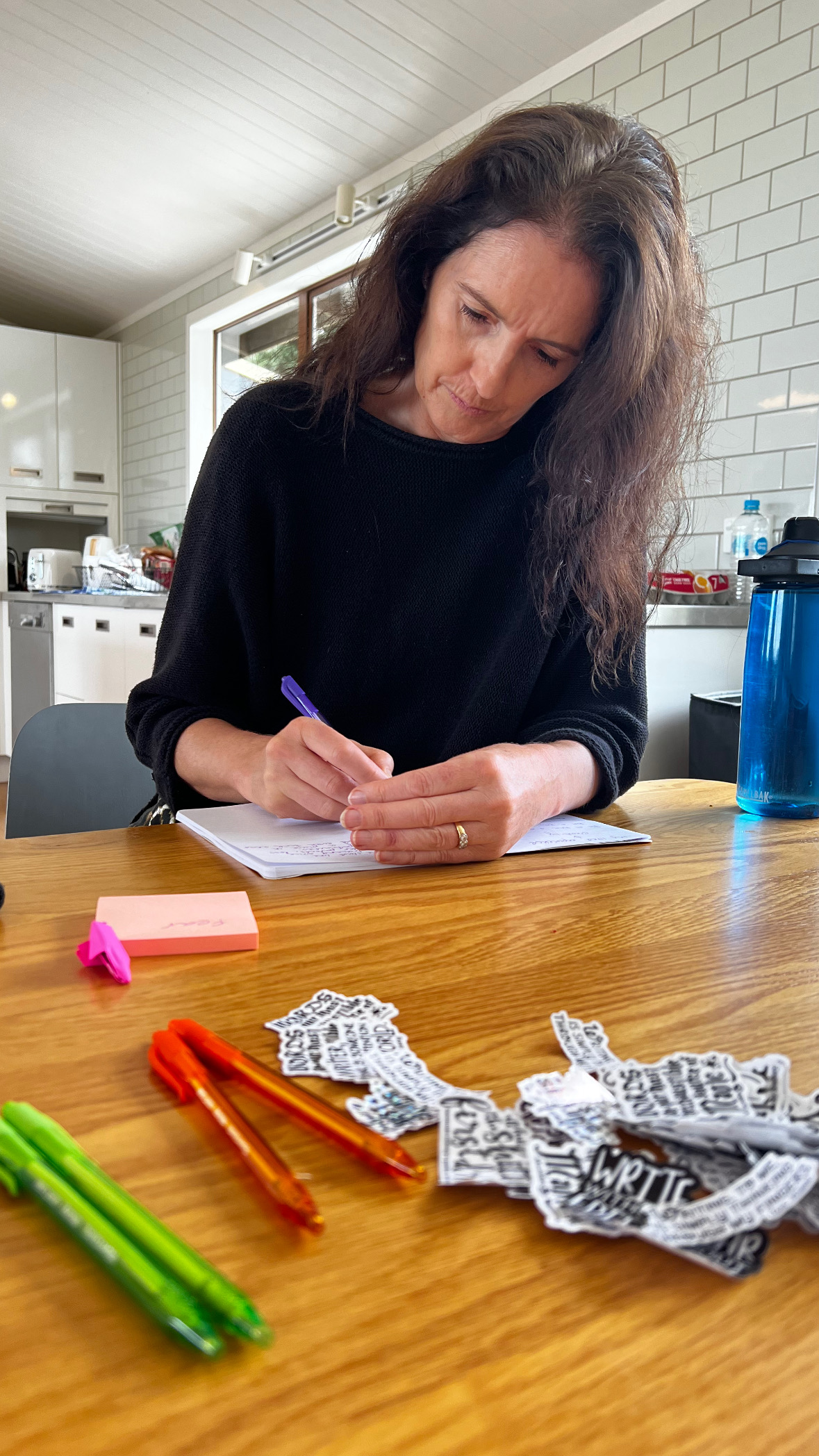 A writer drafting by hand at a table with pens and stickers