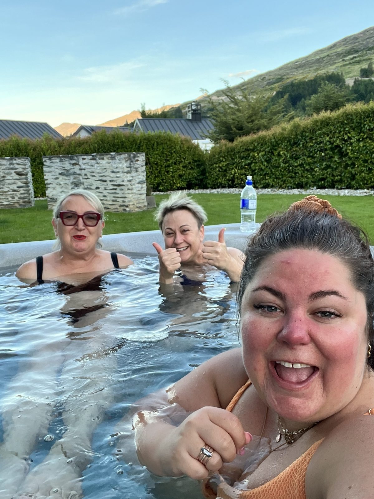 Writers giving a thumbs up from a hot tub with mountains behind them at a Createcation retreat in Queenstown, New Zealand