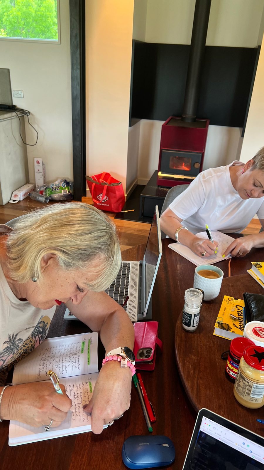 2 writers working at a table by a wood stove during a Createcation retreat in Queenstown