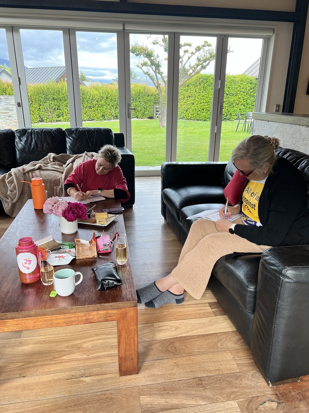 2 writers on leather sofas with notebooks, peonies and bubbles during a Createcation retreat in Queenstown